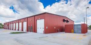 Red, pre-engineered metal building on concrete with blue skies and clouds in background