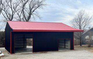 Large, black and red, pre-engineered metal building with trees and blue skies behind it