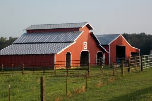 One of many types of metal buildings built for commercial use. It's called a Pole Barn that is red on green grass.