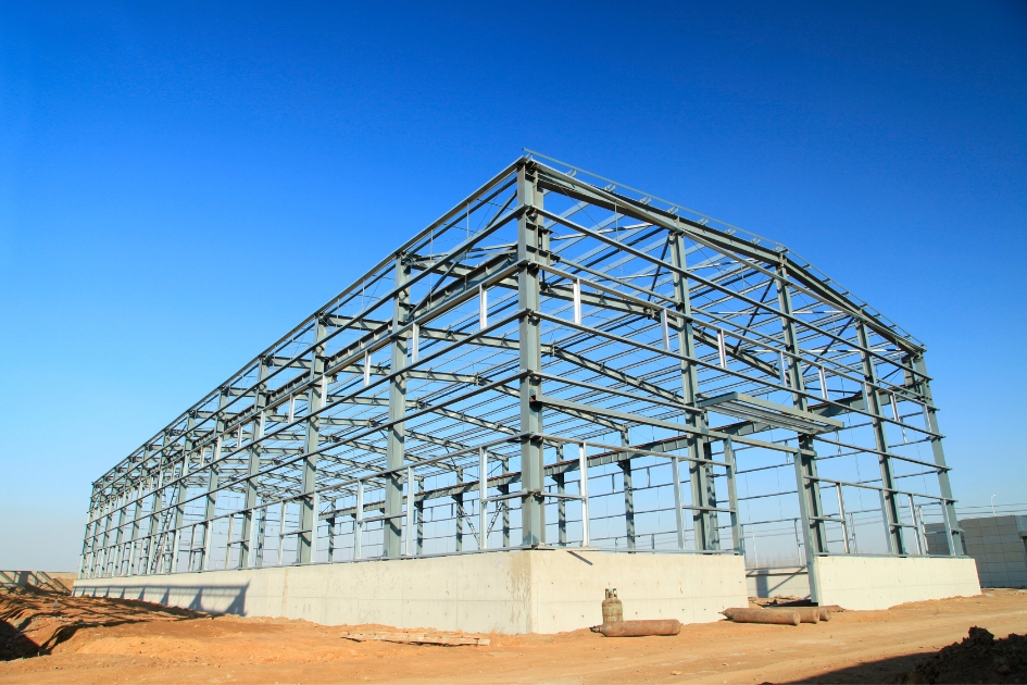 A photo of the beginning of a cold formed metal building process. It's a type of metal building called a steel metal building on a concrete foundation with blue skies behind it