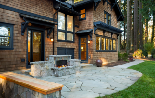 A large brown house with a stamped concrete patio design with a fireplace and warm sunlight.