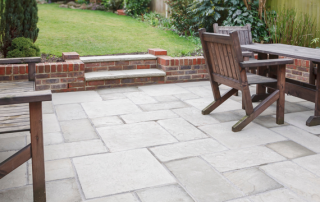 Brown and grey concrete patio design with green grass in the background and brown chairs and a table.