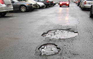 Potholes in a parking lot with cars in the background to help describe tips for parking lot repair